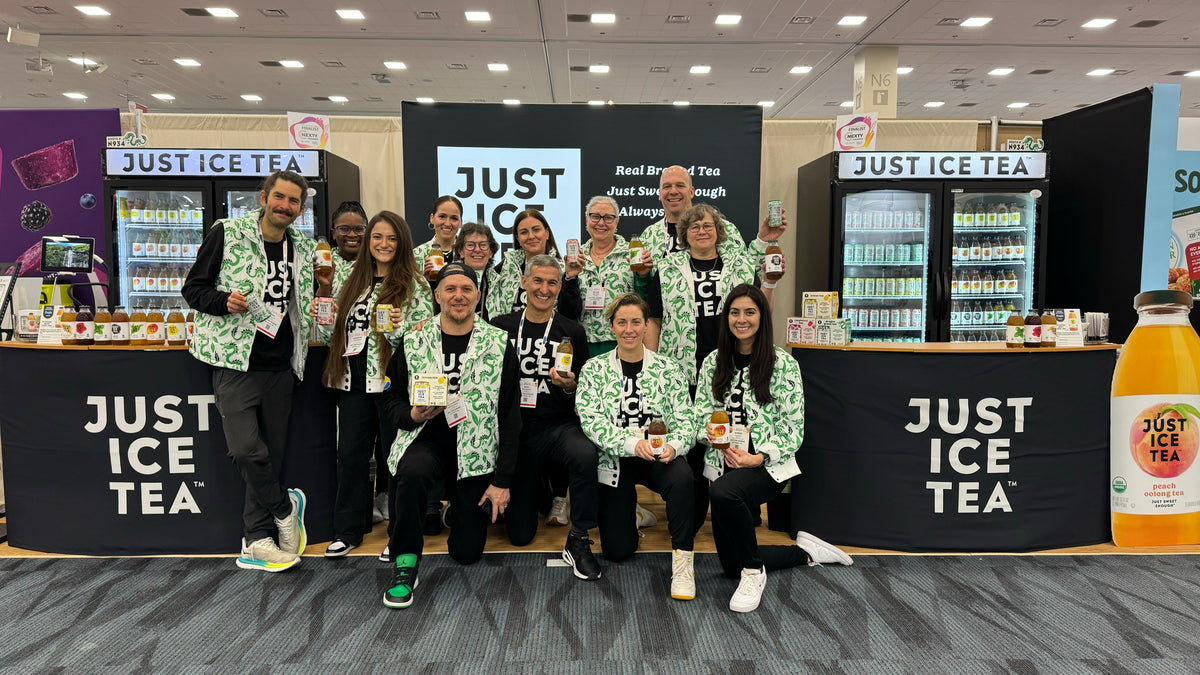 People pose with Just Ice Tea bottles at a trade show booth